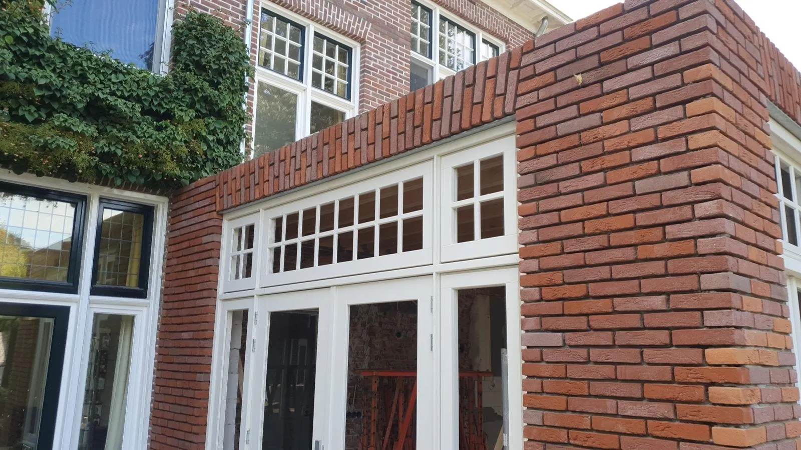 Aanbouw met grote houten puien en rood metselwerk aan een klassieke villa, gebouwd door Danny Nijsten