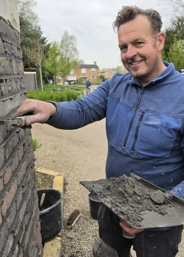 Danny Nijsten met troffel en specie naast een gemetselde muur